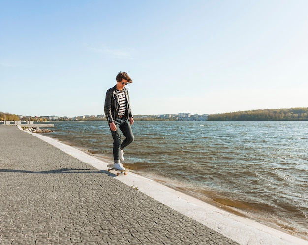 海のそばのスケートボードを持つ若い男