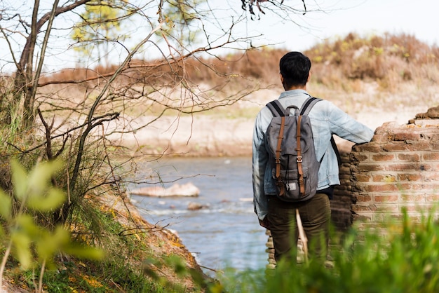 Free photo young man with backpack looking at the lake