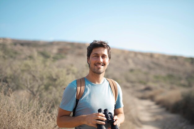 young man with backpack looks the way with binoculars