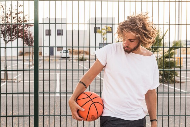Young man with basketball standing against fence