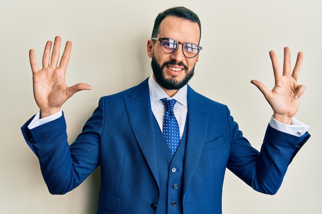 Free photo young man with beard wearing business suit and tie showing and pointing up with fingers number nine while smiling confident and happy.