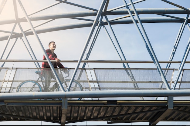 Free photo young man with bicycle on bridge