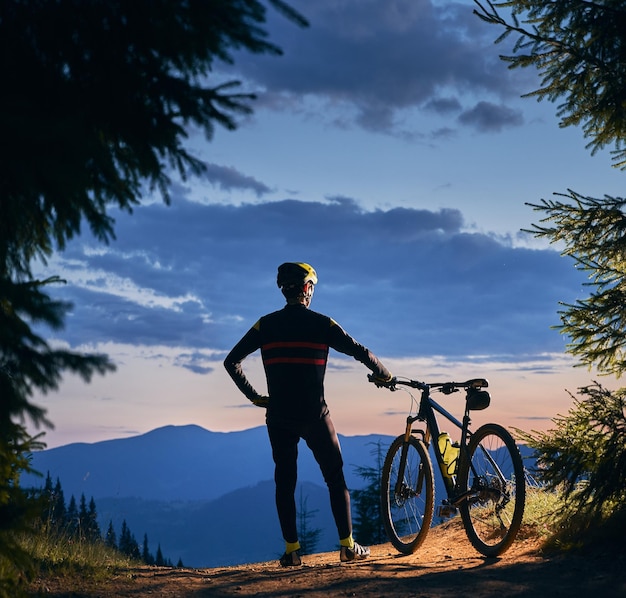 Foto gratuita giovane con una bicicletta che si gode il tramonto in montagna