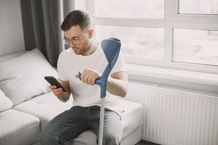 Free Photo young man with broken leg at home. using smartphone.