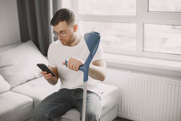 Young man with broken leg at home. Using smartphone.