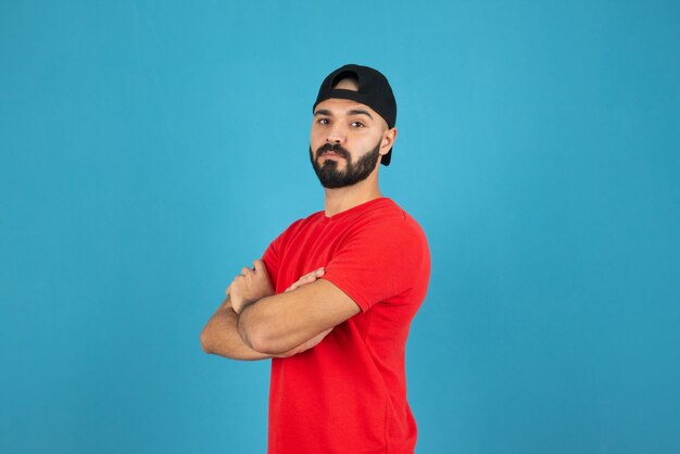 Young man with cap wearing red t-shirt standing with crossed arms . 