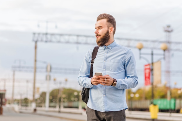 Молодой человек с мобильным телефоном стоит на железнодорожной станции