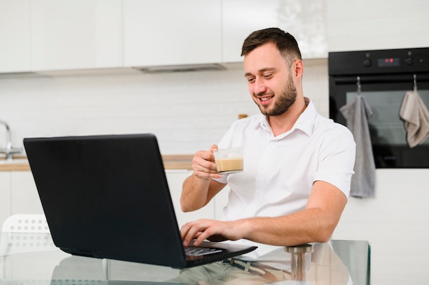 Young man with coffee smiling at laptop