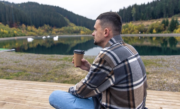 山のぼかした背景に一杯のコーヒーを持つ若い男