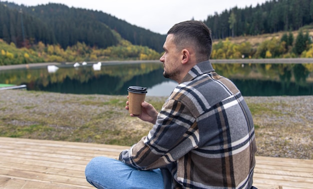 Молодой человек с чашкой кофе на размытом фоне гор