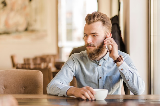 Young man with cup of coffee talking on cellphone in caf�