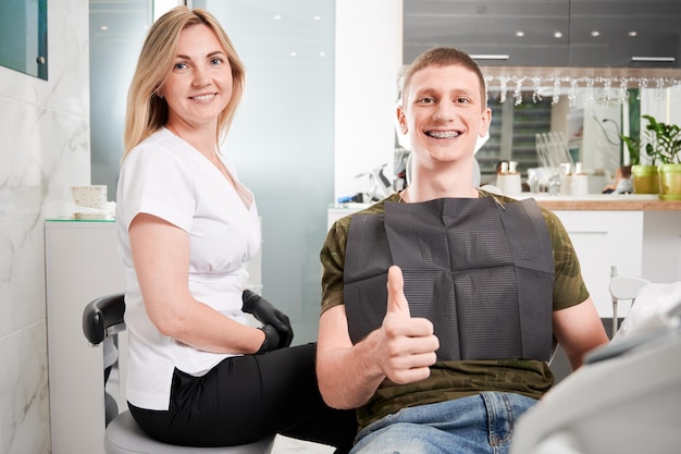 Young man with dental braces at dentist office sitting in dentist chair