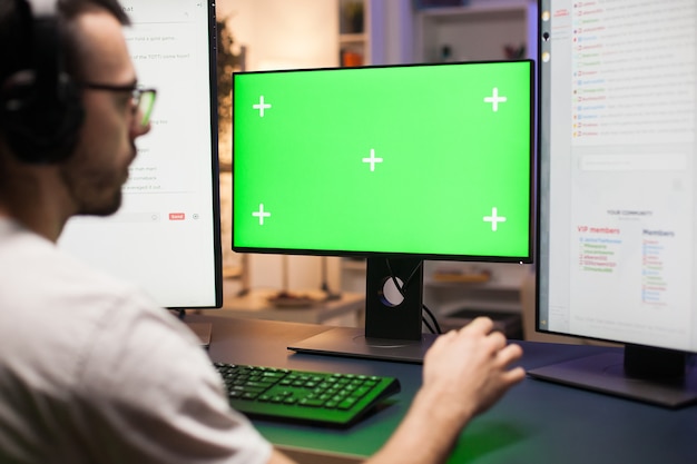 Young man with eyeglasses playing games on computer with green mock up while streaming.