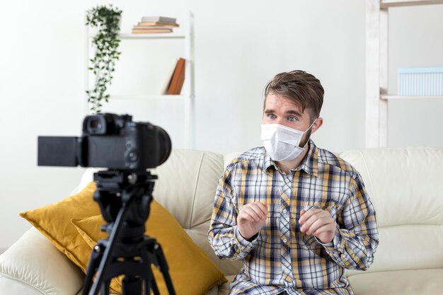 Young man with face mask recording video at home