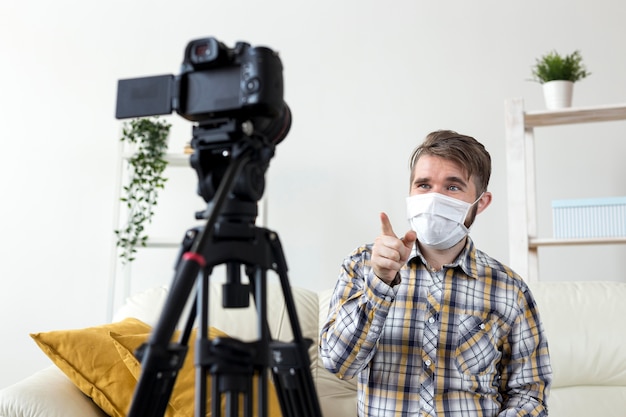 Young man with face mask recording video at home