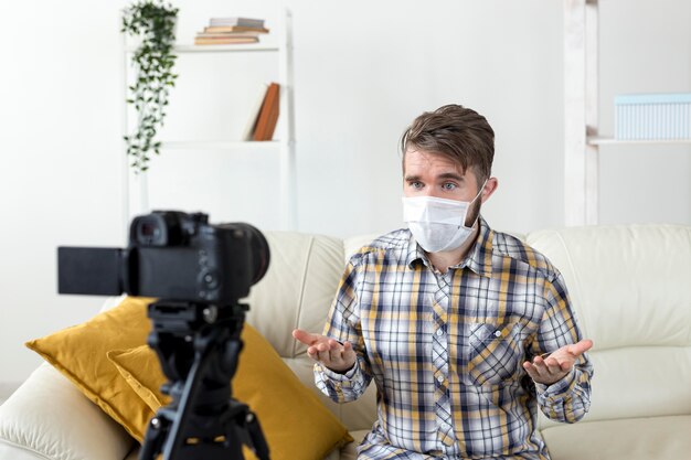 Young man with face mask recording video at home