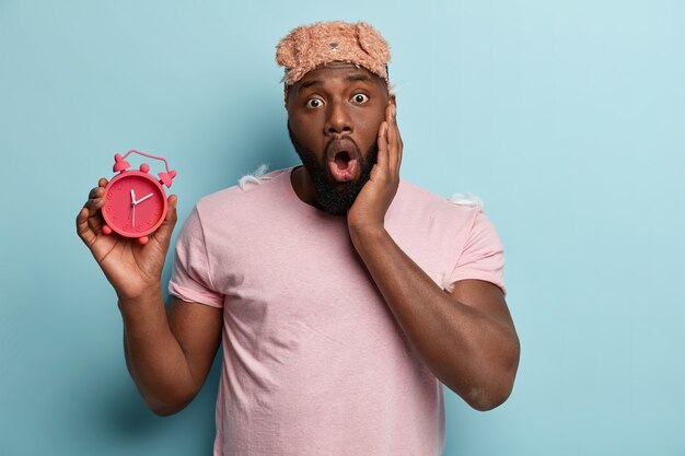 Young man with feathers on T-shirt holding alarm clock