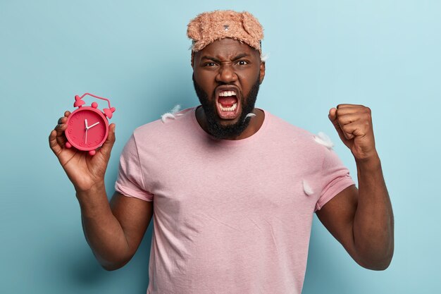 Young man with feathers on T-shirt holding alarm clock