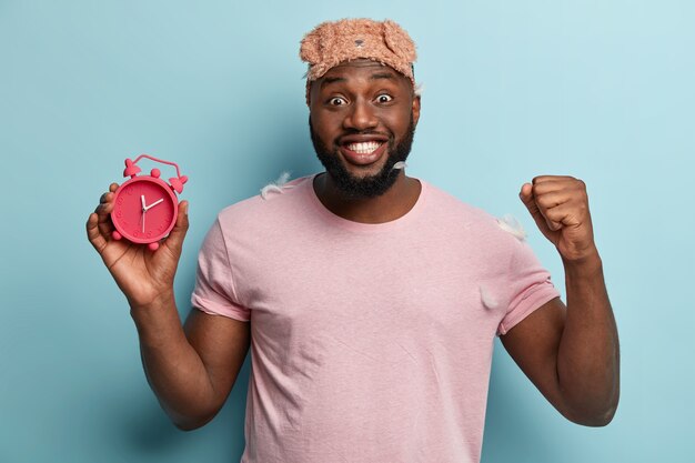 Young man with feathers on T-shirt holding alarm clock