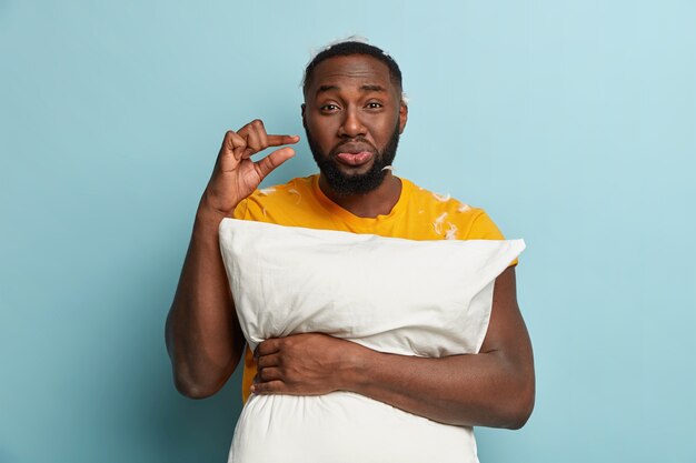 Young man with feathers on T-shirt holding pillow