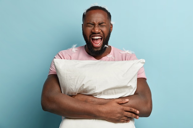 Young man with feathers on T-shirt holding pillow