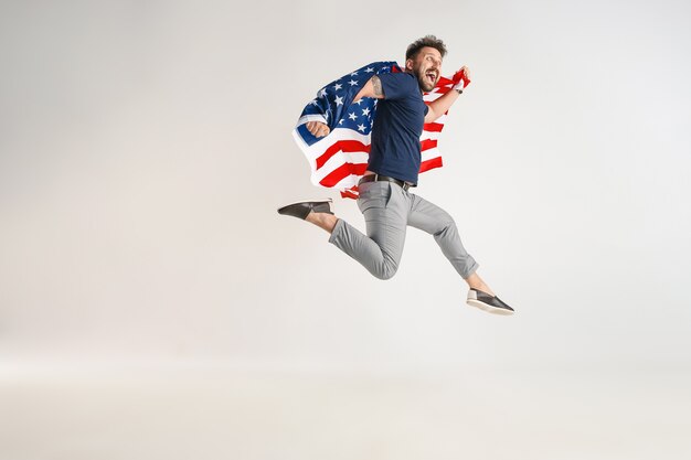 Young man with  flag of the United States of America jumping isolated on white studio.