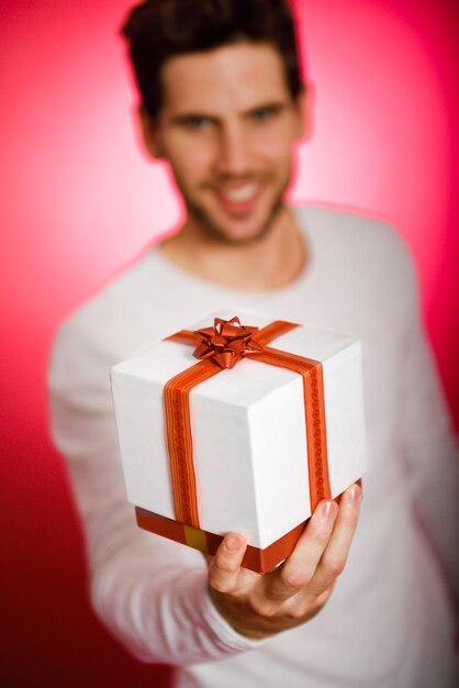 Free photo young man with a gift box with red ribbon on red background