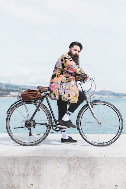 Foto gratuita giovane uomo con la sua bicicletta sul frangiflutti vicino alla costa