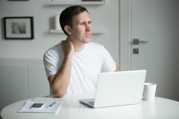 Young man with his hands at his neck, sitting near desk