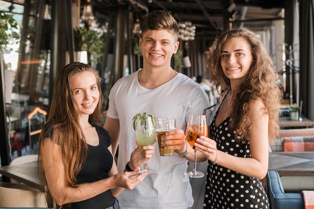 Young man with his two female friends holding glasses of drinks