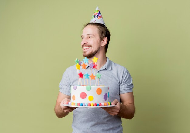 밝은 벽에 행복하고 흥분 생일 파티를 축하하는 생일 케이크를 들고 휴가 모자와 젊은 남자