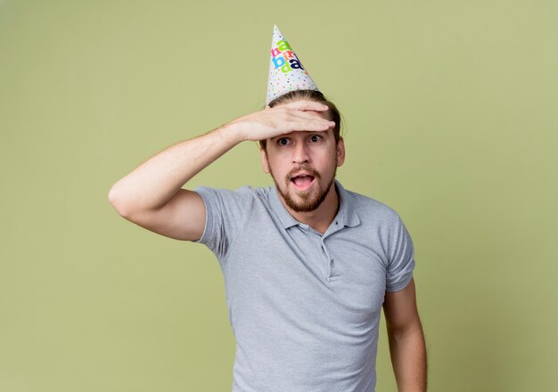 Giovane uomo con cappello vacanza guardando lontano con la mano sopra la testa sorpreso in piedi sopra la parete leggera