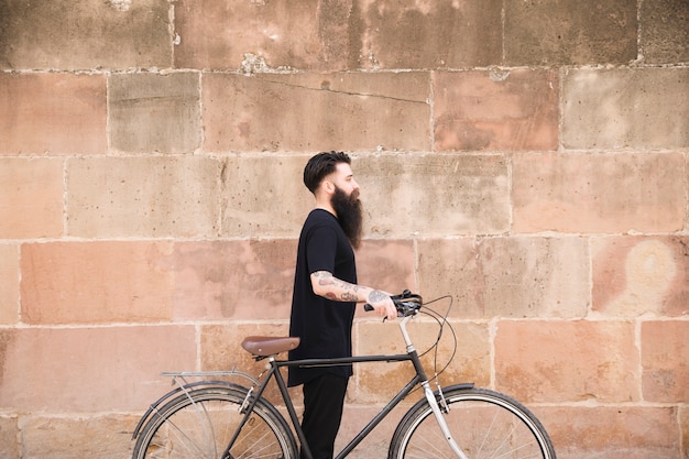 Free photo young man with long bearded man standing with bicycle against wall