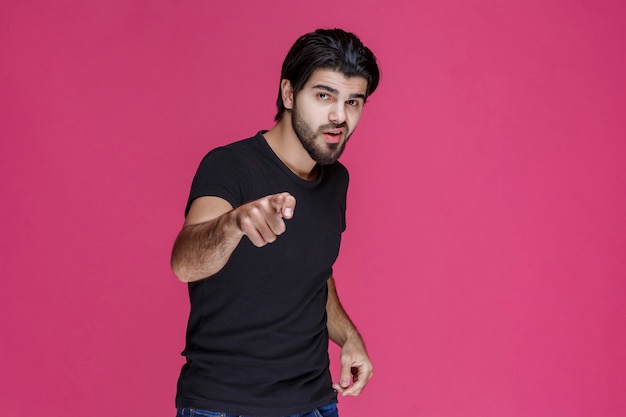 Young man with long hairs and beard showing or pointing at something with his fingers.