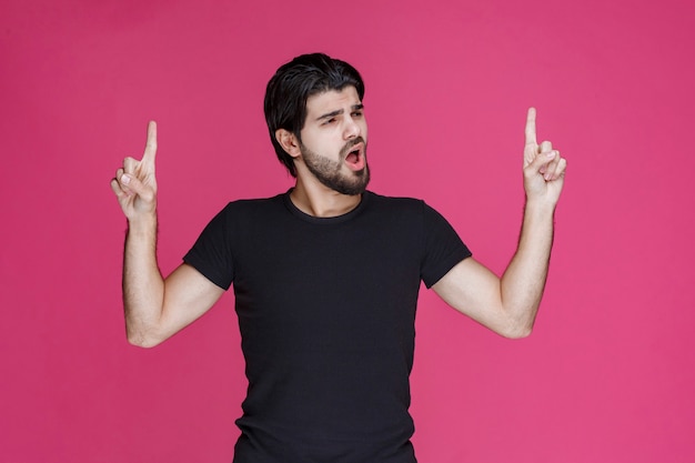 Young man with long hairs and beard showing or pointing at something with his fingers.