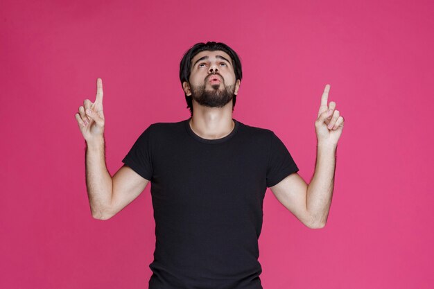 Young man with long hairs and beard showing or pointing at something with his fingers.