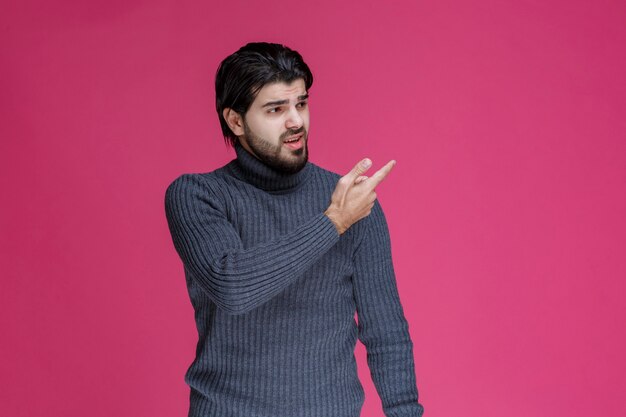 Young man with long hairs and beard showing or pointing at something with his fingers.