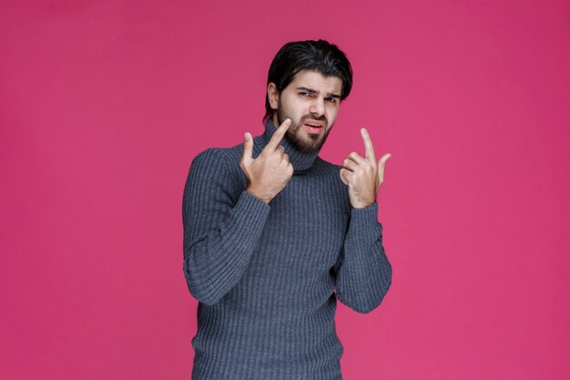 Young man with long hairs and beard showing or pointing at something with his fingers.