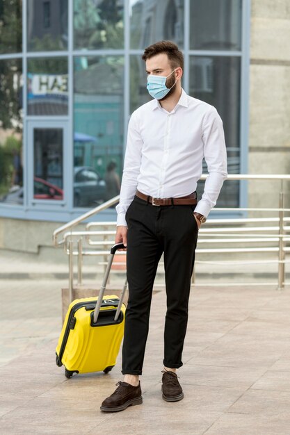 Young man with luggage wearing mask