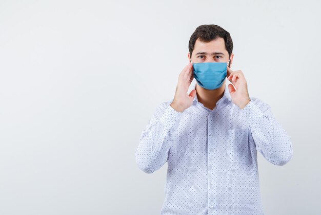 The young man  with medical mask is looking at camera on white background