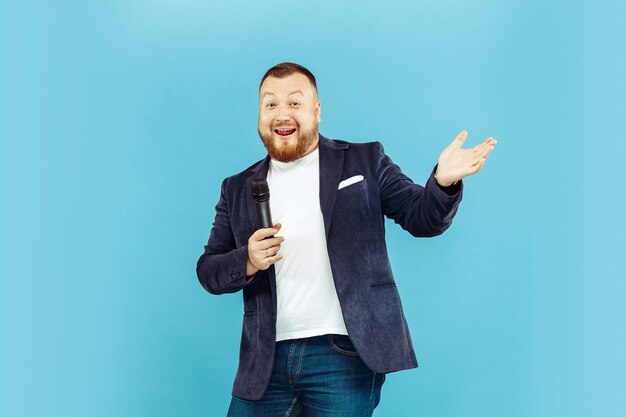 Young man with microphone on blue studio, leading concept.