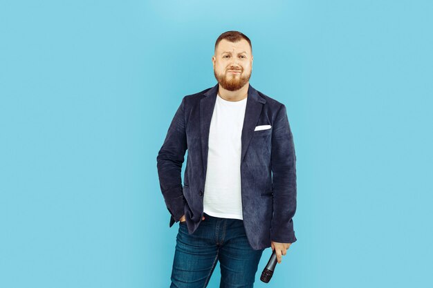 Young man with microphone on blue studio, leading concept.