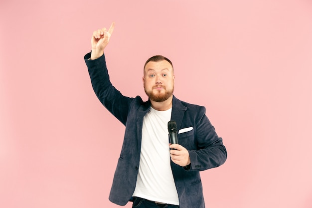 Young man with microphone on pink background, leading with microphone