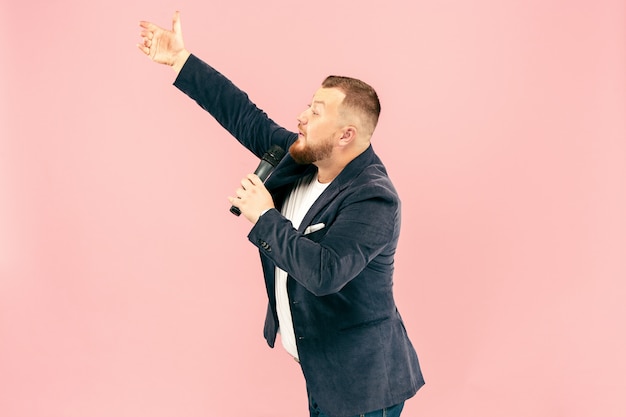 Young man with microphone on pink space, leading with microphone