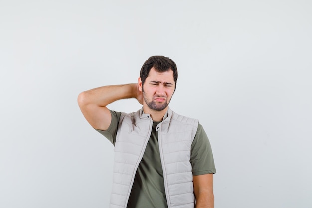 Foto gratuita il giovane con mal di collo sta mettendo la mano dietro il collo su sfondo bianco