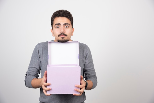 A young man with an opened purple box over a white wall .