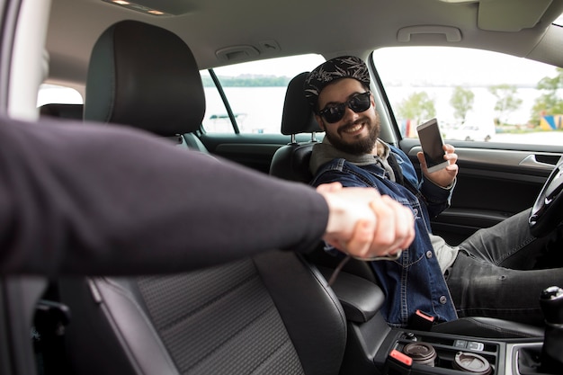 Young man with phone greeting friend while sitting in car