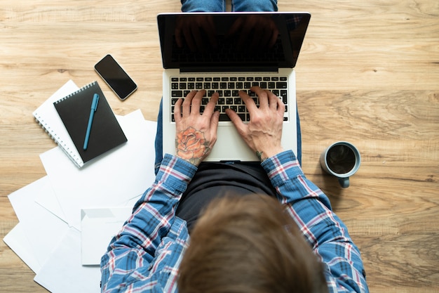 Young man with rose tattoo on hand typing on laptop