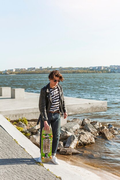 海のそばのスケートボードを持つ若い男