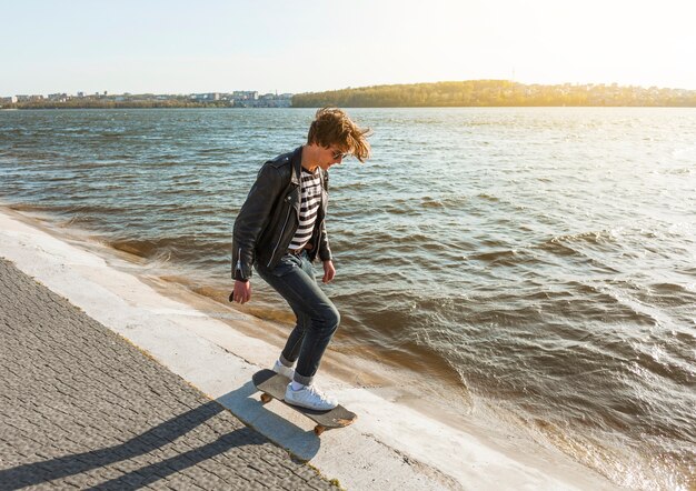 海のそばのスケートボードを持つ若い男